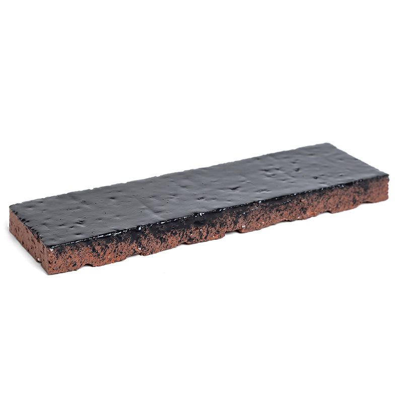A 2x8 glazed brick in Abyss, shot at an angle so the red clay body shows on the cut edge