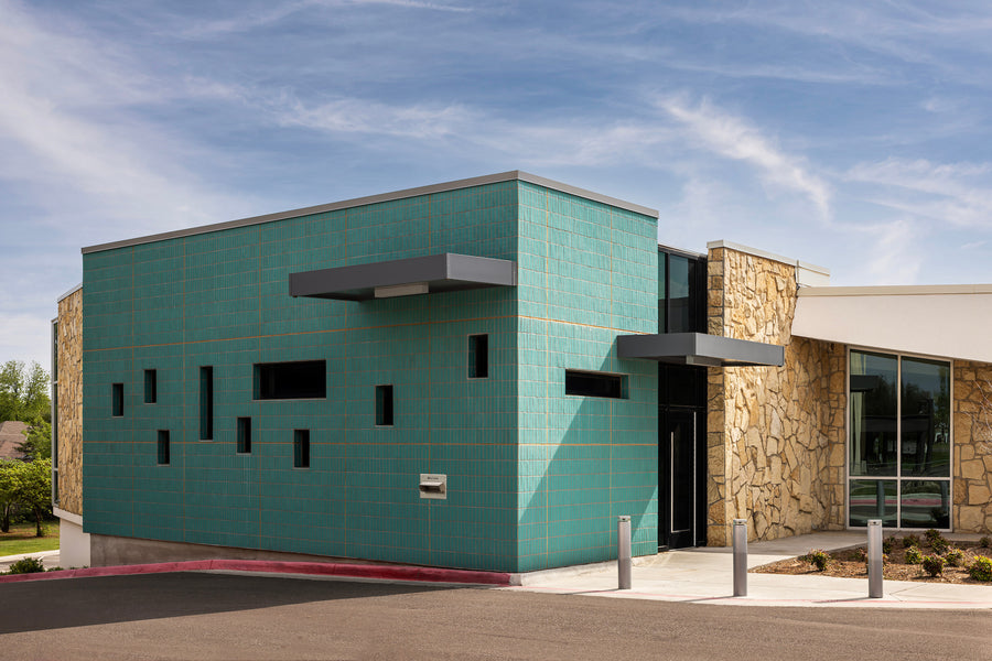 The teal glazed brick volume at Belle Isle Library in daylight, vertical stack bond against rough stone