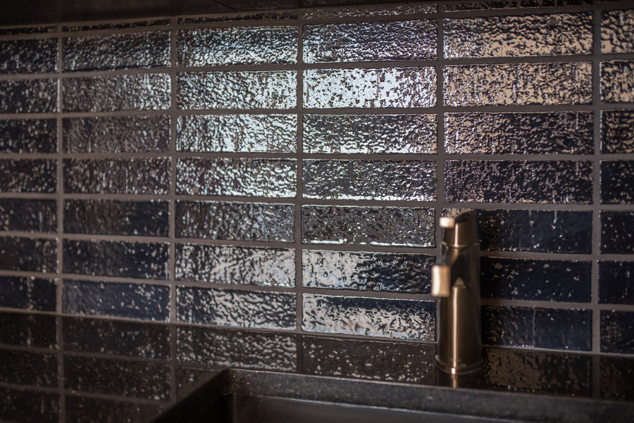 A bathroom wall of glazed brick in Oxford Blue behind a stone basin, running bond with a dark joint