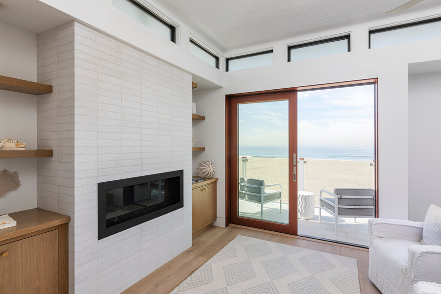 A fireplace wall of glazed brick in Pure White in a beach house, running bond, with the ocean through the door