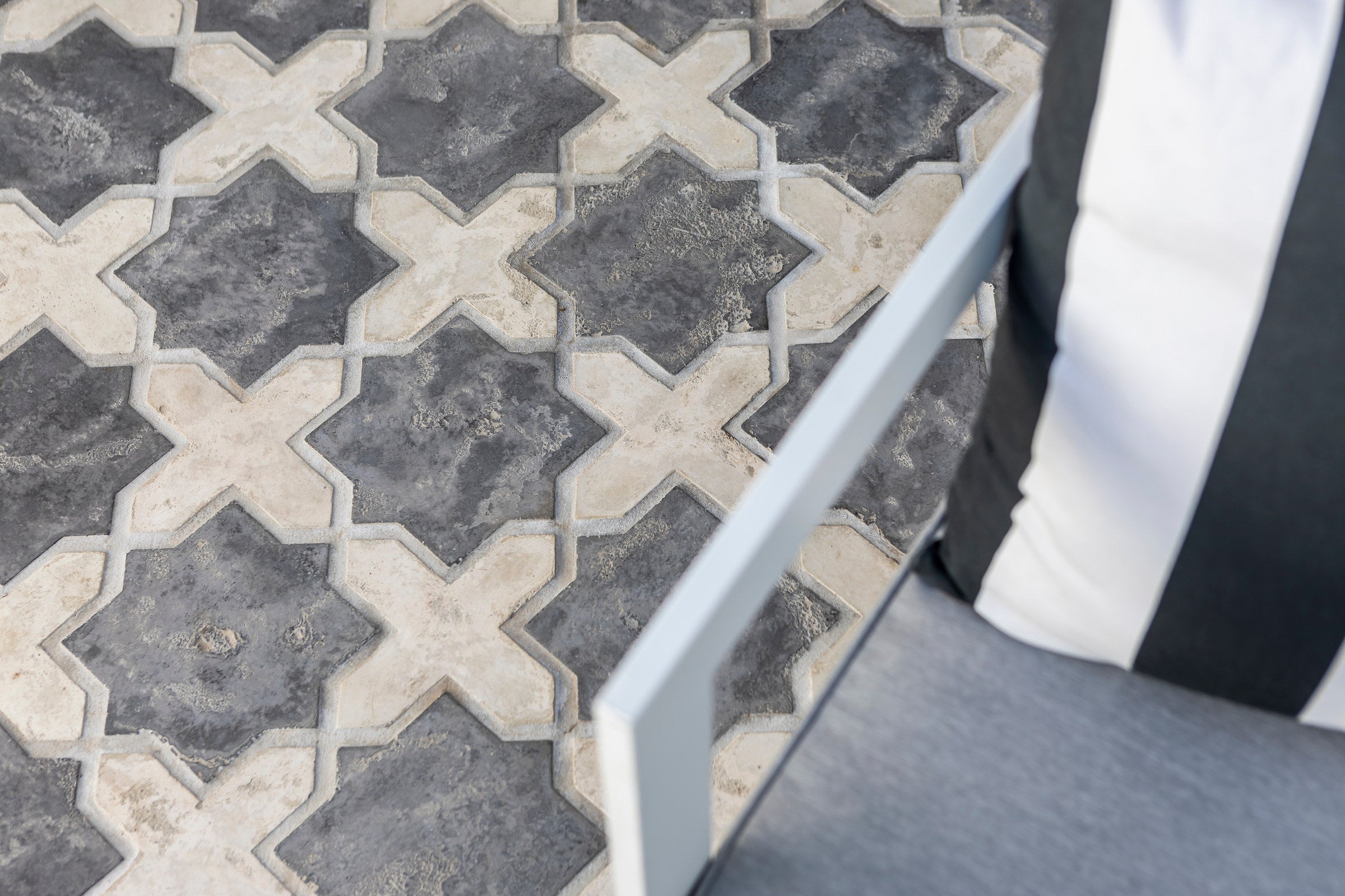 A floor of ARTO star and cross tile in cream and charcoal, seen close, with the edge of a white table and a striped cushion beside it