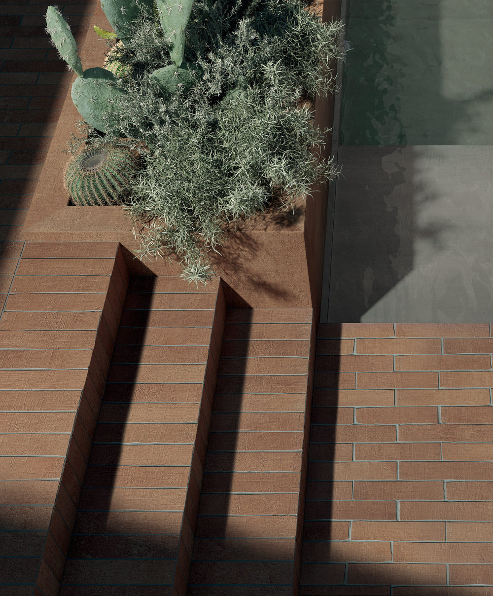 Outdoor steps and low walls clad in narrow Terra Crea plank tile in the warm Cotto color, with a barrel cactus and a silver shrub in the planter above and hard afternoon shadows across the treads