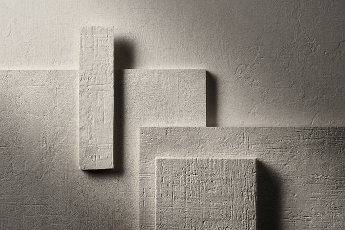 A studio arrangement of Terra Crea porcelain pieces in Bianco, the palest of the five, lit hard from the side against a dark ground