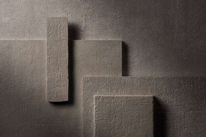 The same arrangement of Terra Crea pieces in Grafite, a mid grey, lit hard from the side against a dark ground