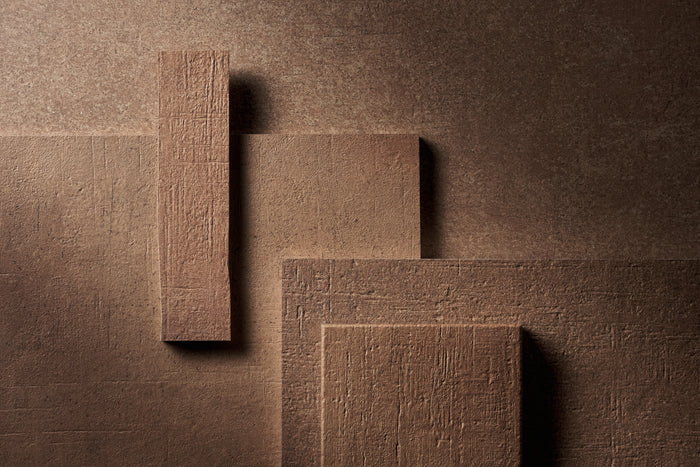 The same arrangement of Terra Crea pieces in Cotto, a warm baked earth red, lit hard from the side against a dark ground