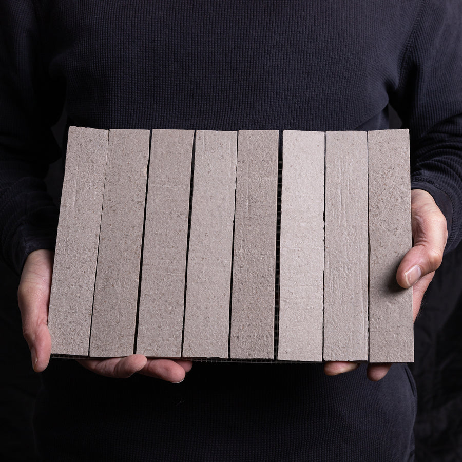A person in dark clothes holding a Terra Crea mosaic sheet of eight 8x12 planks in Duna, turned edge on so the thickness shows