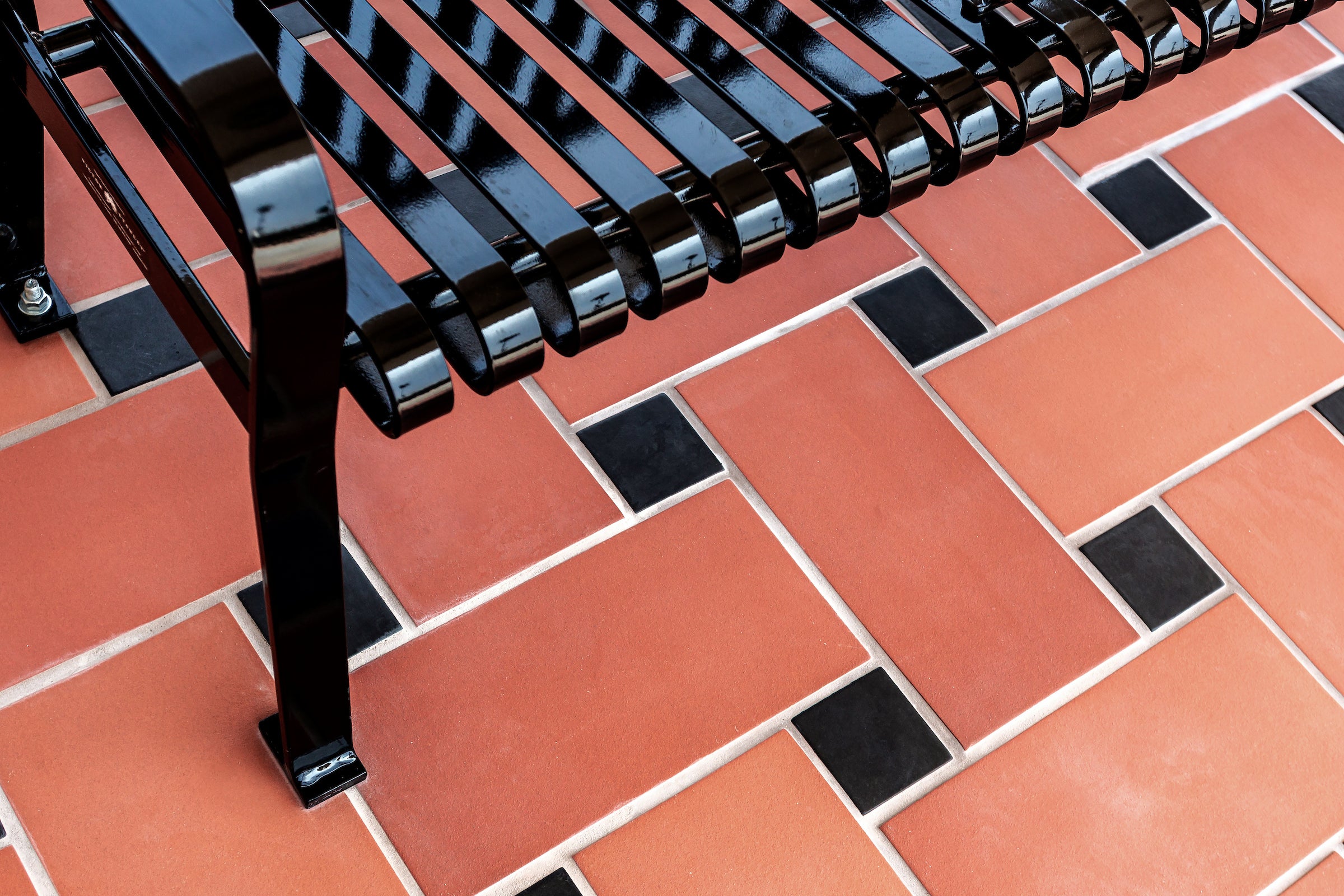 Monrovia rectangles laid in a running bond with small black square inserts at the joints, a black slatted bench standing on them