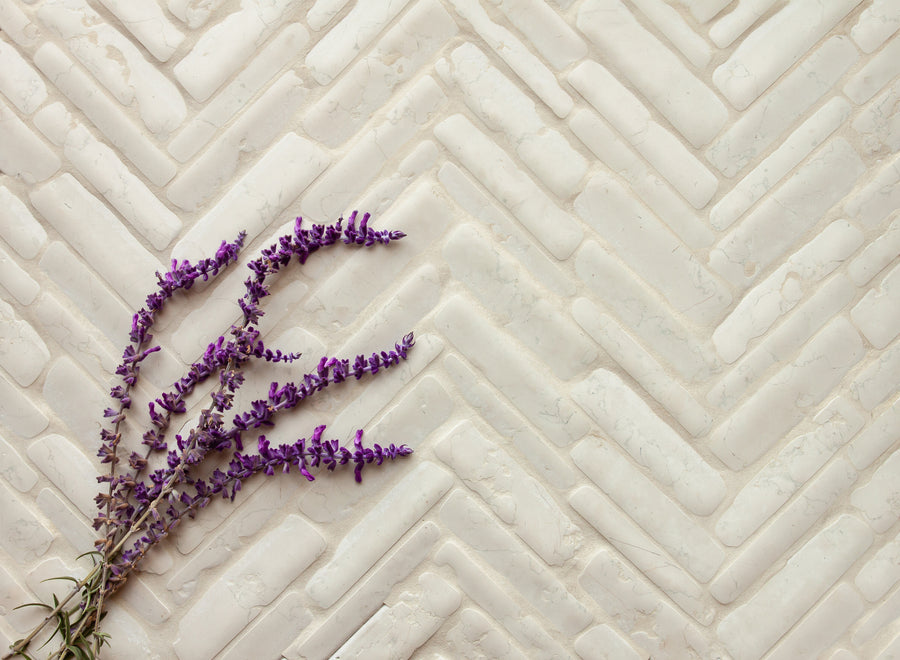 Small rectangular marble pieces laid in a herringbone run, pale and softly rounded, with a sprig of lavender lying across them